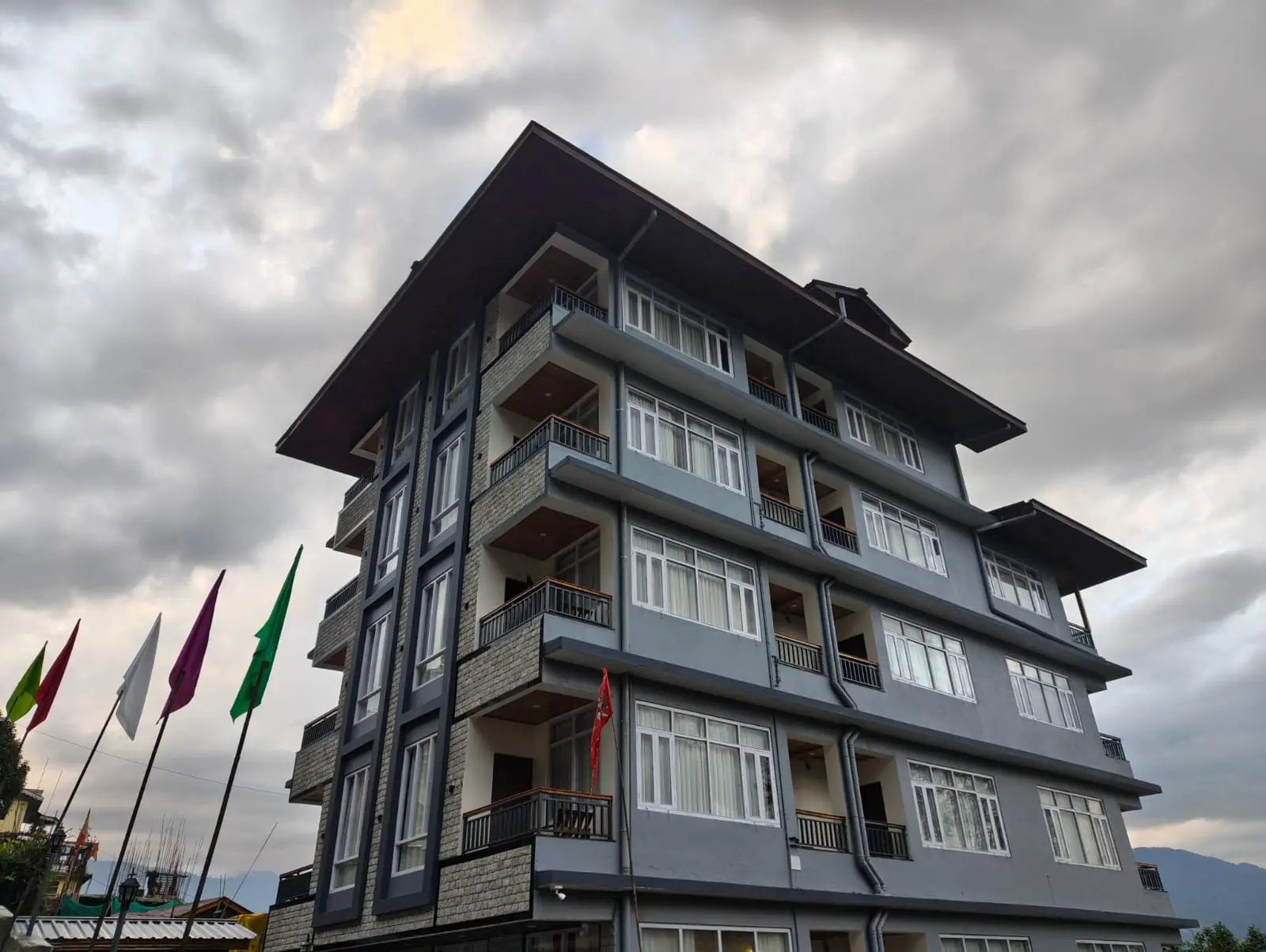 The Asian Hills building in Pelling, prayer flags in the foreground under a monsoon sky